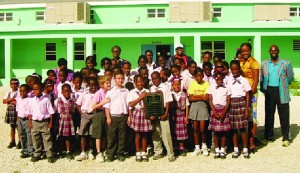 Commonwealth Games athlete, Desiree Cocks (back-left), Board Members, Althea Hodge (back-centre) and Cardigan Connor (right) and coach, Derrick Carty (back-centre-right) presents the Commonwealth Sports Day Shield to Yellow House at Alwyn Allison Richardson Primary School.